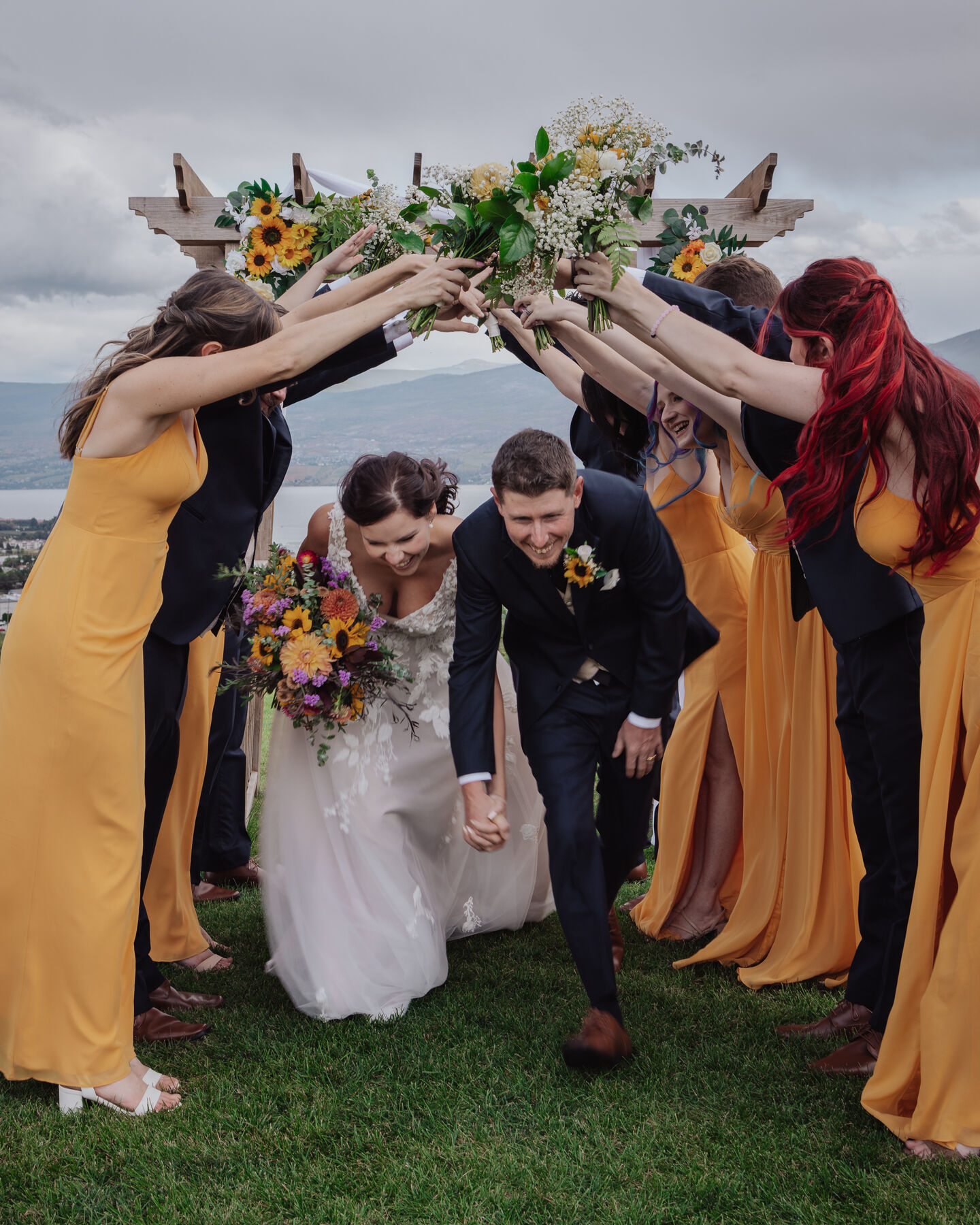 Bride and groom ducking under an arch of flowers held by the wedding party