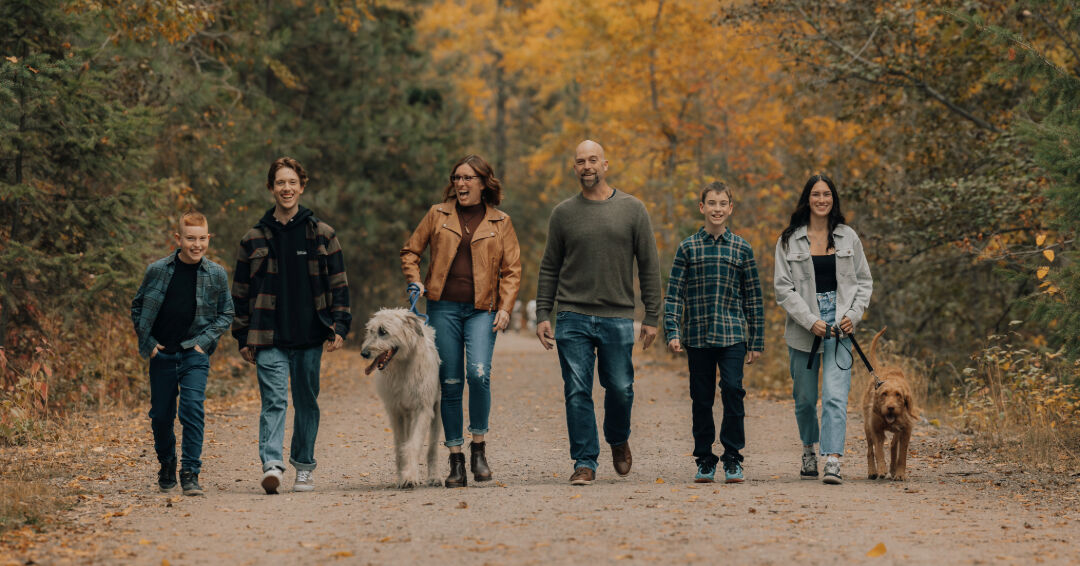 Family of six and two dogs walking toward the camera on an autumn path