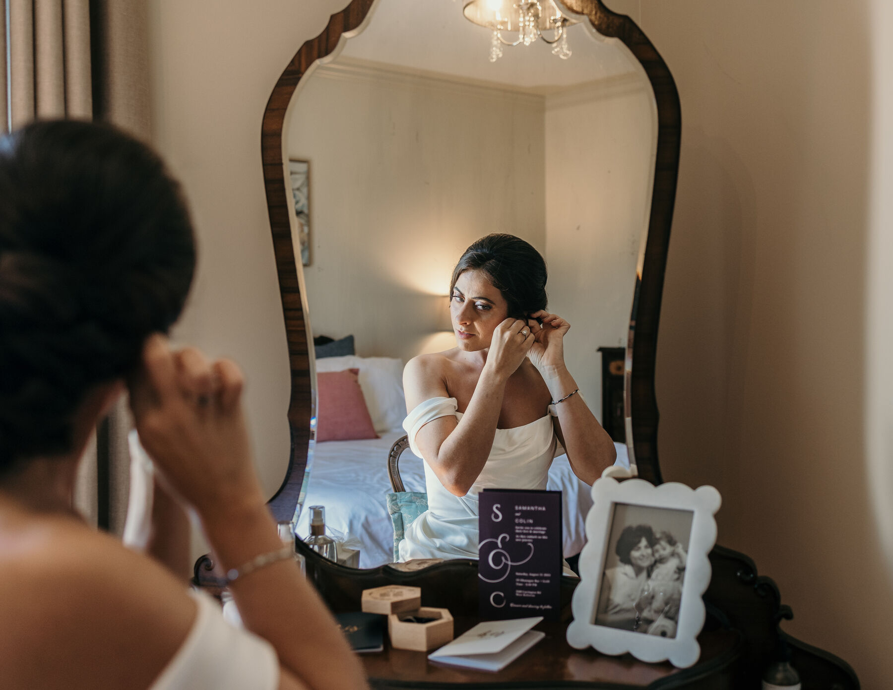 Bride putting in an earring in front of an antique mirror