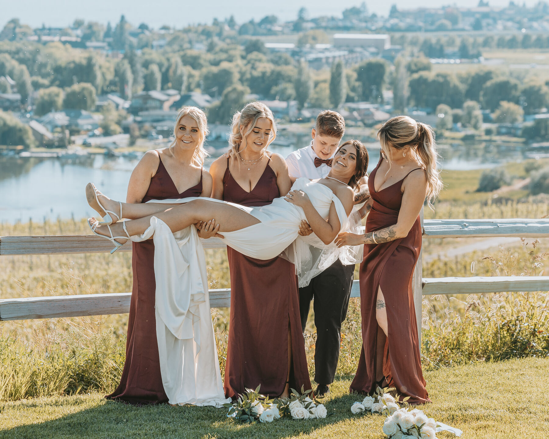 Bridesmaids and the groom laughing as they carry the bride across their arms
